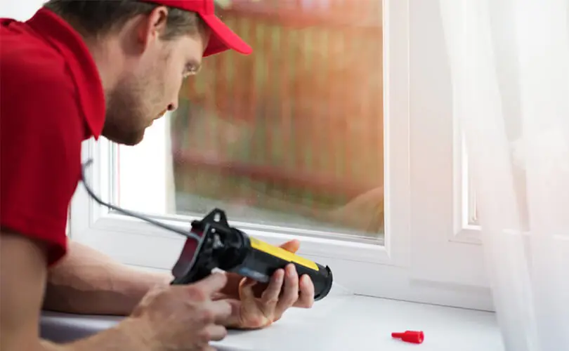 A worker caulks around a window.